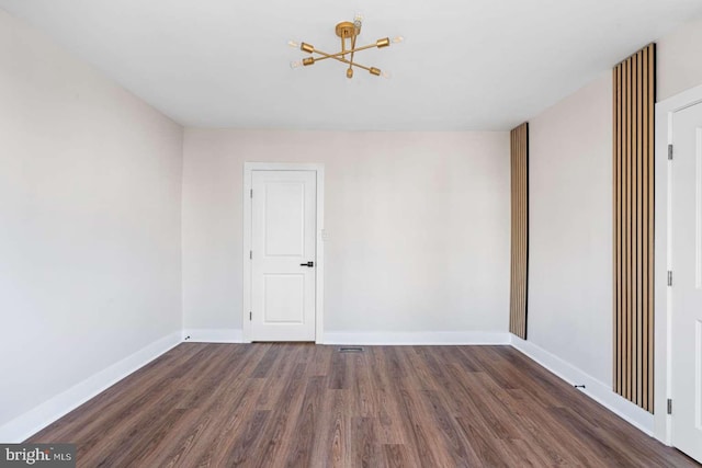 empty room with a chandelier, baseboards, and wood finished floors