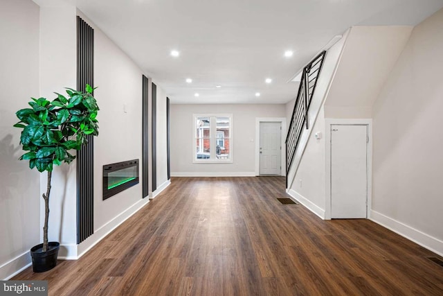 unfurnished living room with dark wood-style floors, visible vents, baseboards, recessed lighting, and stairs