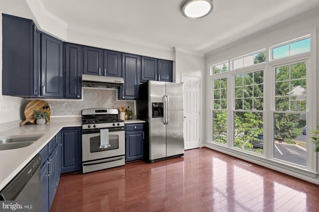 kitchen with appliances with stainless steel finishes, under cabinet range hood, blue cabinets, light countertops, and crown molding