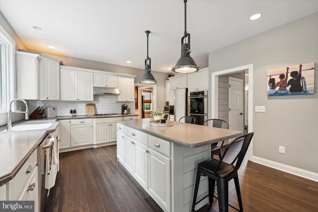 kitchen with tasteful backsplash, under cabinet range hood, a breakfast bar, appliances with stainless steel finishes, and a sink