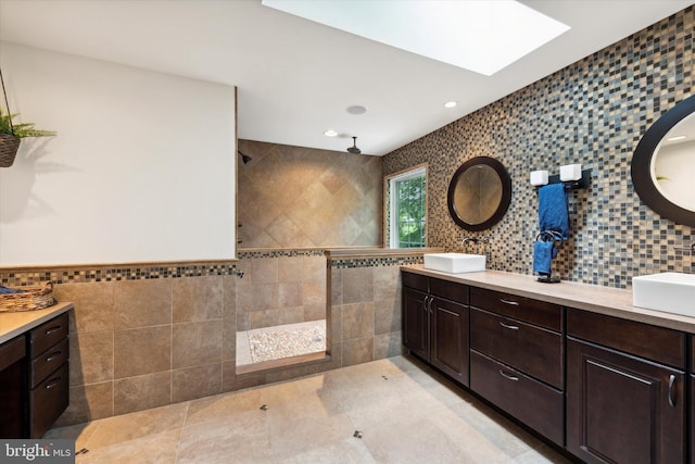 bathroom featuring a skylight, tiled shower, tile walls, and a sink