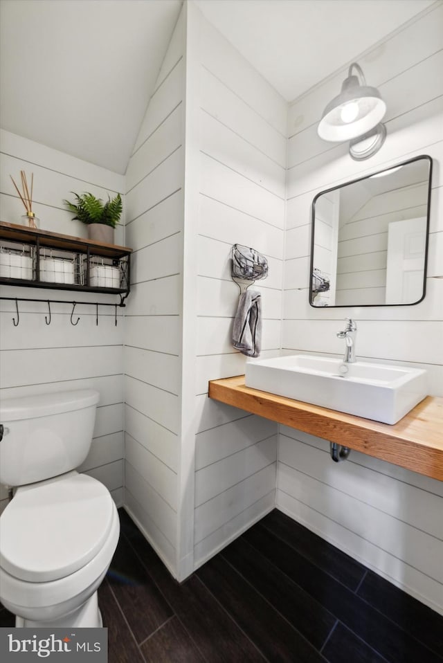 bathroom with vaulted ceiling, toilet, wood finished floors, and a sink