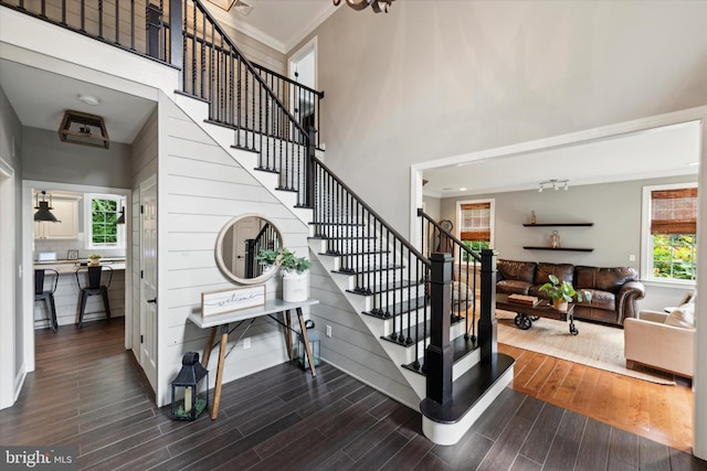 staircase with wood finished floors, a towering ceiling, and ornamental molding