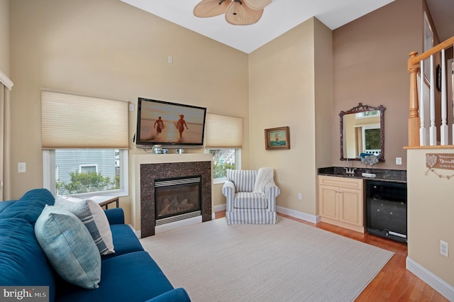 living room with beverage cooler, baseboards, a ceiling fan, light wood-style flooring, and a glass covered fireplace