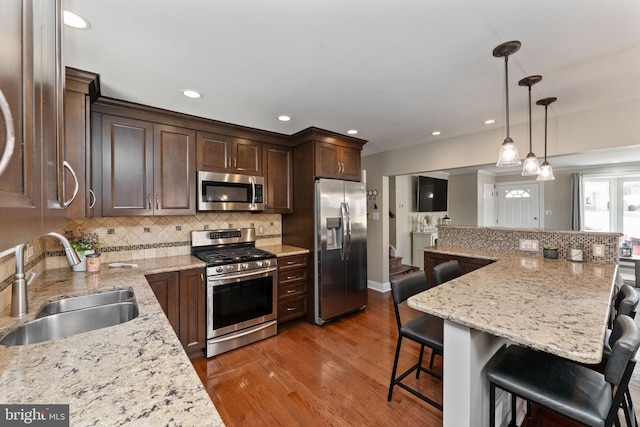 kitchen with a sink, a kitchen breakfast bar, dark brown cabinetry, appliances with stainless steel finishes, and wood finished floors