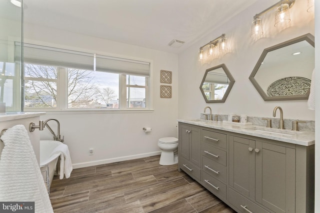 bathroom with baseboards, wood finished floors, double vanity, and a sink