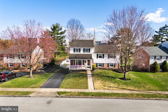 traditional home featuring brick siding, covered porch, aphalt driveway, and a front lawn