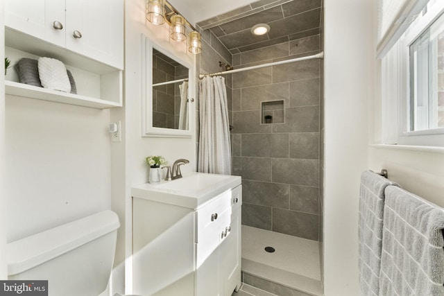 bathroom with a tile shower, toilet, and vanity