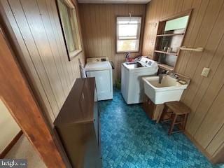 clothes washing area featuring laundry area, independent washer and dryer, wood walls, and a sink