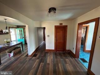 unfurnished dining area featuring baseboards, arched walkways, and dark wood-type flooring