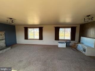 unfurnished living room featuring carpet flooring, a fireplace with raised hearth, and a healthy amount of sunlight