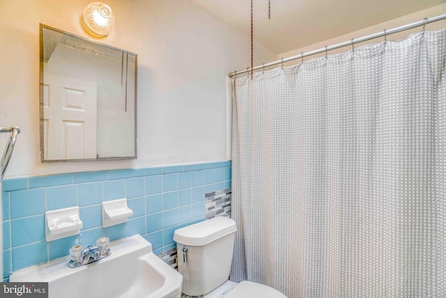 bathroom featuring a shower with shower curtain, wainscoting, a sink, and toilet