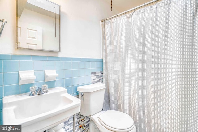 full bath with a shower with curtain, a sink, tile walls, toilet, and wainscoting