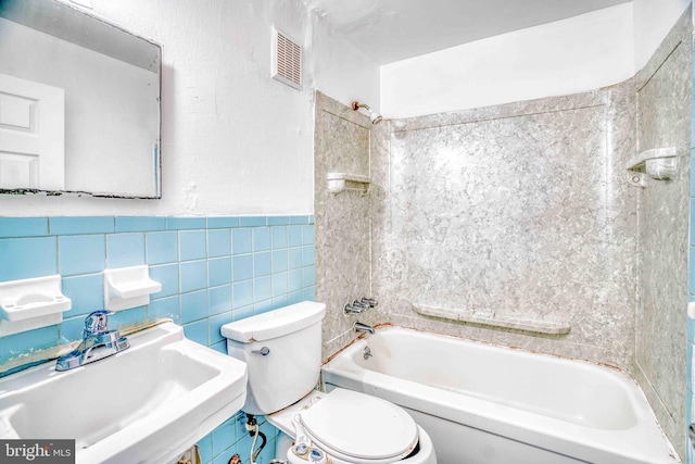 bathroom with shower / bath combination, toilet, visible vents, tile walls, and a sink