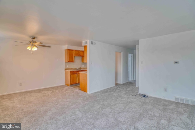 unfurnished living room featuring ceiling fan, visible vents, light carpet, a sink, and baseboards