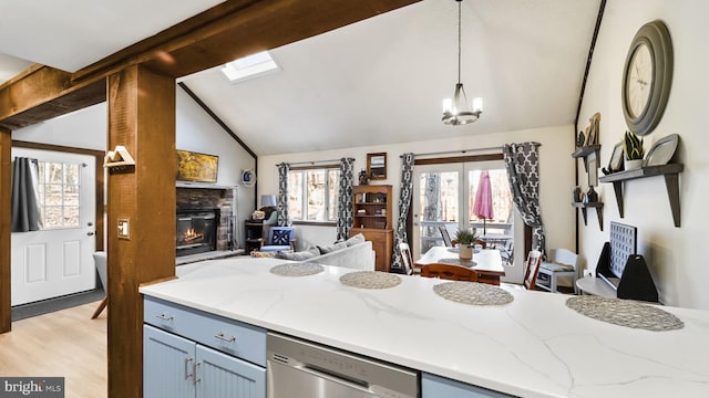 kitchen featuring light stone countertops, vaulted ceiling, stainless steel dishwasher, decorative light fixtures, and open floor plan