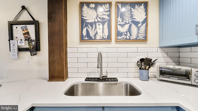 kitchen with blue cabinets, a sink, backsplash, a toaster, and light stone countertops