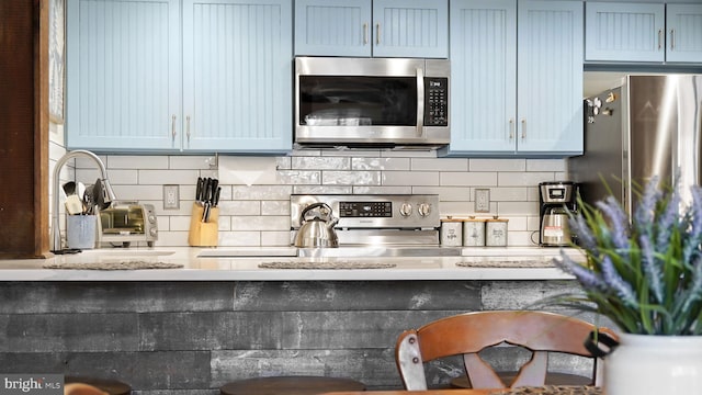 kitchen featuring blue cabinets, stainless steel microwave, and backsplash