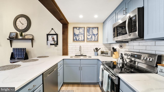 kitchen with tasteful backsplash, light wood finished floors, light stone countertops, appliances with stainless steel finishes, and a sink