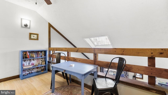 home office with baseboards, lofted ceiling with skylight, light wood-style flooring, a textured ceiling, and a ceiling fan