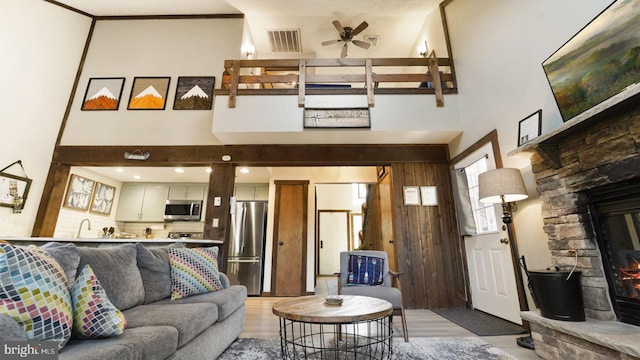 living room with visible vents, a stone fireplace, a high ceiling, and ceiling fan