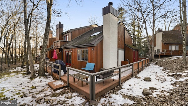 snow covered rear of property featuring a chimney and a wooden deck