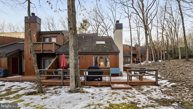 snow covered house with a wooden deck and a chimney