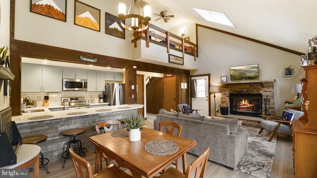 dining area with ornamental molding, a stone fireplace, a skylight, light wood-style floors, and high vaulted ceiling