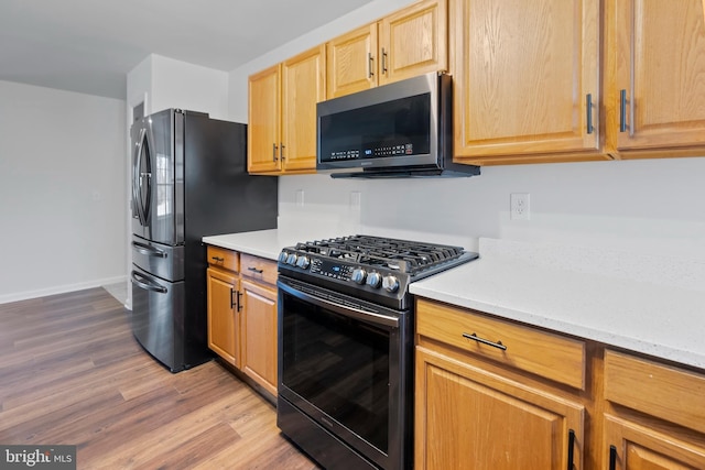 kitchen with baseboards, light brown cabinetry, light stone counters, wood finished floors, and stainless steel appliances