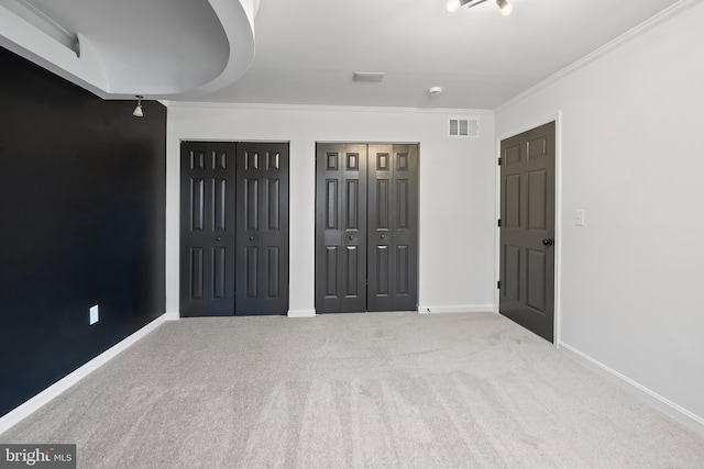 unfurnished bedroom with visible vents, crown molding, baseboards, multiple closets, and carpet floors