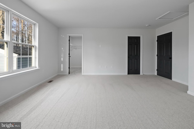 unfurnished bedroom featuring visible vents, carpet floors, baseboards, attic access, and a spacious closet