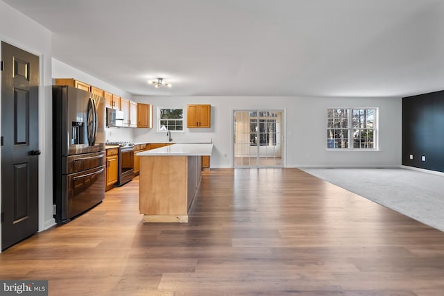 kitchen with a sink, open floor plan, a center island, appliances with stainless steel finishes, and light countertops