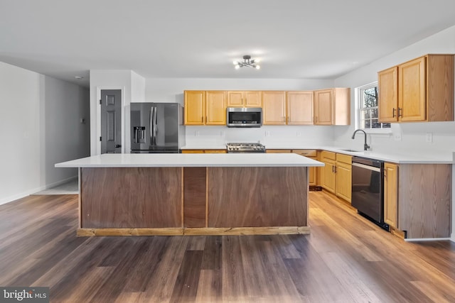 kitchen featuring wood finished floors, a kitchen island, a sink, light countertops, and appliances with stainless steel finishes