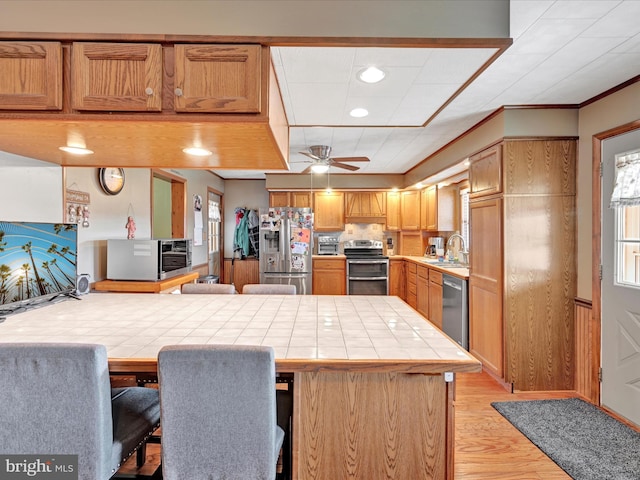 kitchen with a peninsula, a sink, ceiling fan, tile counters, and stainless steel appliances