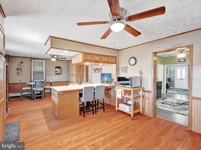 kitchen featuring light wood-style floors, baseboard heating, ceiling fan, and wainscoting