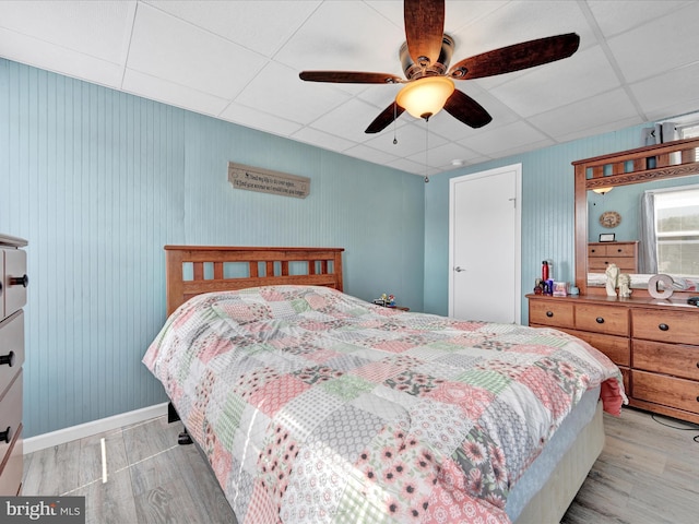 bedroom featuring baseboards, light wood-type flooring, a drop ceiling, and ceiling fan