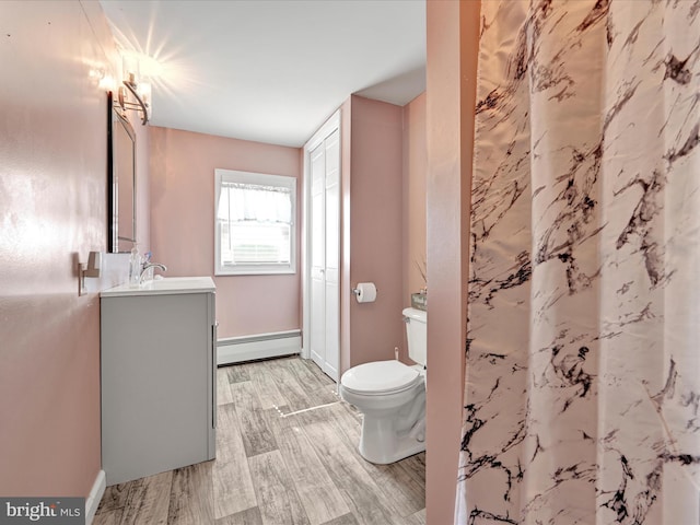 bathroom featuring toilet, a baseboard heating unit, wood finished floors, baseboards, and vanity