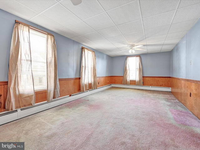 carpeted spare room with wooden walls, a paneled ceiling, a ceiling fan, and wainscoting