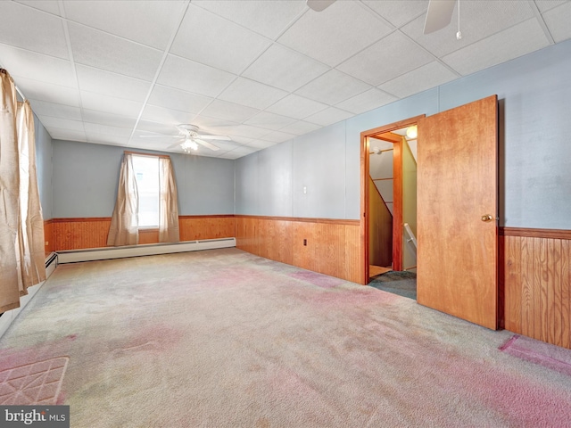 empty room with wainscoting, wood walls, a ceiling fan, and a baseboard radiator