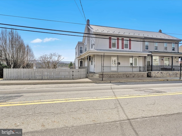 view of property featuring a fenced front yard, covered porch, a chimney, and metal roof