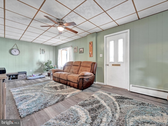 living room featuring a paneled ceiling, a baseboard heating unit, ceiling fan, and wood finished floors