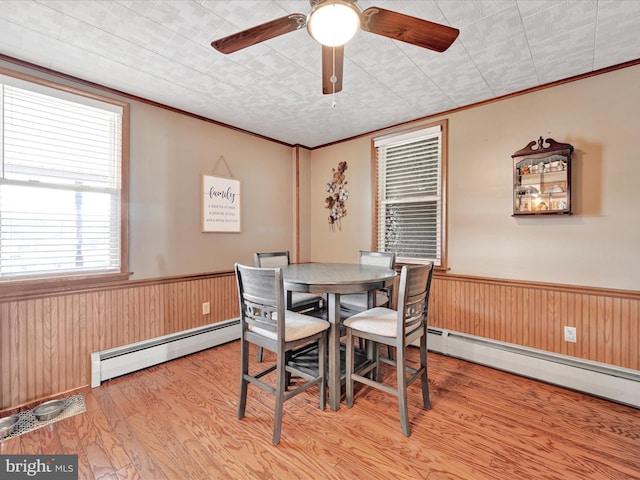 dining space with baseboard heating, wood finished floors, wainscoting, and wood walls