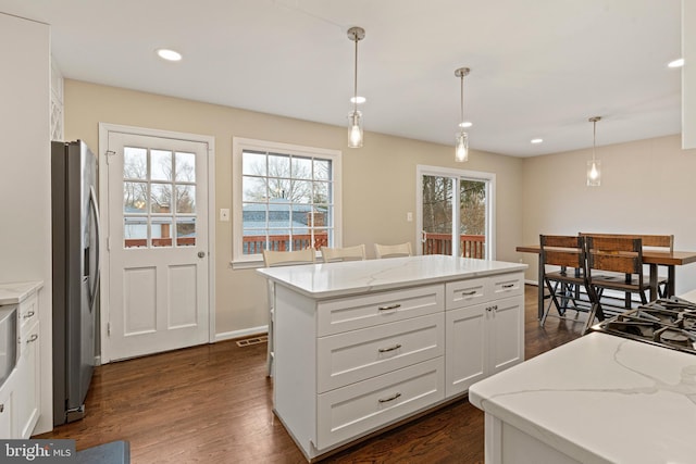 kitchen featuring a kitchen island, dark wood-type flooring, hanging light fixtures, stainless steel fridge, and white cabinetry