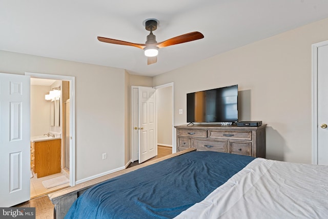 bedroom featuring a ceiling fan, wood finished floors, baseboards, a sink, and connected bathroom