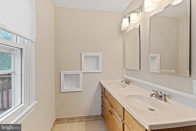 full bath featuring tile patterned flooring, double vanity, baseboards, and a sink