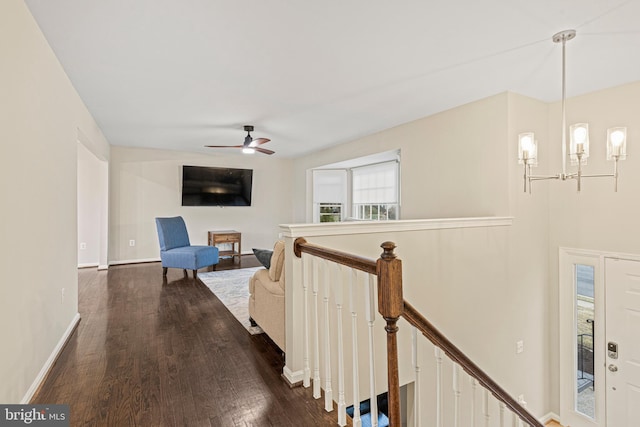 interior space featuring dark wood finished floors, ceiling fan with notable chandelier, an upstairs landing, and baseboards