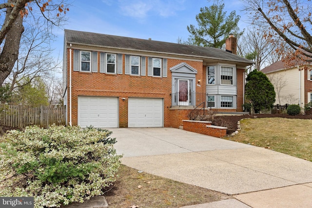 bi-level home with brick siding, concrete driveway, a chimney, and fence