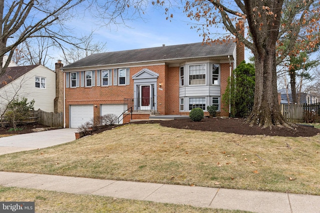 raised ranch featuring brick siding, a front lawn, fence, concrete driveway, and an attached garage