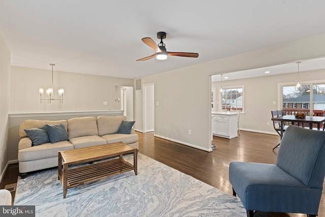 living area with dark wood finished floors, visible vents, ceiling fan with notable chandelier, and baseboards