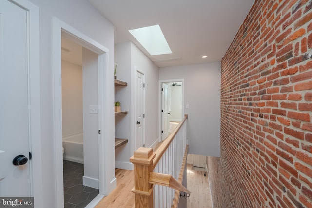 hall featuring brick wall, a skylight, an accent wall, and wood finished floors